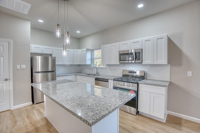 kitchen with sink, a kitchen island, decorative light fixtures, white cabinets, and appliances with stainless steel finishes