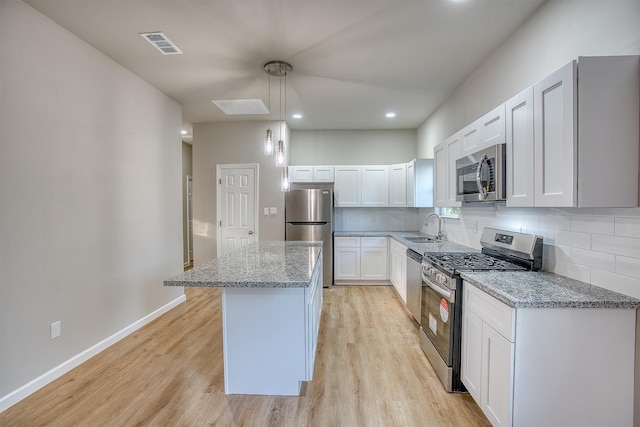 kitchen featuring stainless steel appliances, sink, decorative light fixtures, white cabinets, and a center island