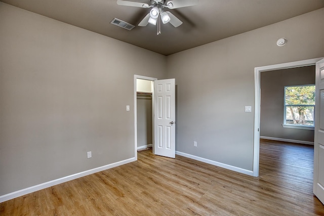 unfurnished bedroom with a closet, ceiling fan, light hardwood / wood-style flooring, and a walk in closet