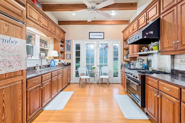 kitchen with high end range, sink, beam ceiling, light hardwood / wood-style flooring, and dark stone countertops