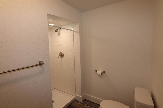 bathroom with baseboards, toilet, a stall shower, and wood finished floors
