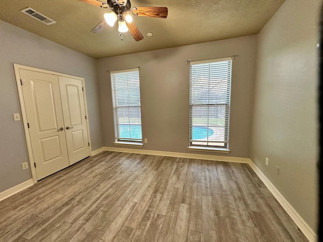 spare room with a ceiling fan, wood finished floors, visible vents, baseboards, and a textured ceiling