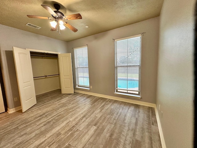 unfurnished bedroom featuring visible vents, baseboards, a textured ceiling, and wood finished floors