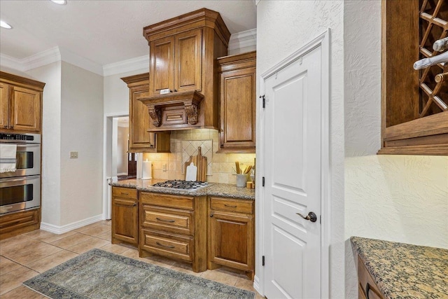 kitchen with ornamental molding, dark stone counters, brown cabinets, tasteful backsplash, and stainless steel appliances