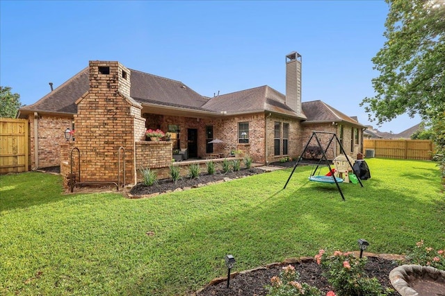 rear view of house featuring a shingled roof, brick siding, a fenced backyard, a chimney, and a lawn