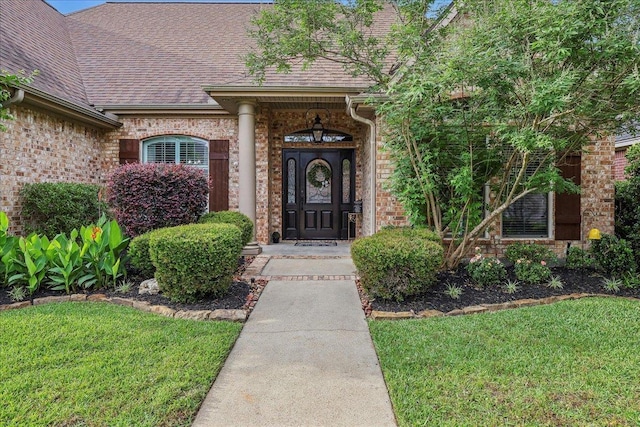 entrance to property featuring a lawn, brick siding, and a shingled roof