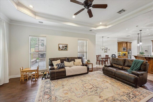 living room featuring visible vents, ornamental molding, a raised ceiling, and ceiling fan with notable chandelier