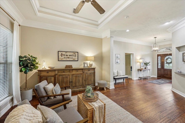 living area with dark wood-style flooring, baseboards, ornamental molding, and ceiling fan with notable chandelier
