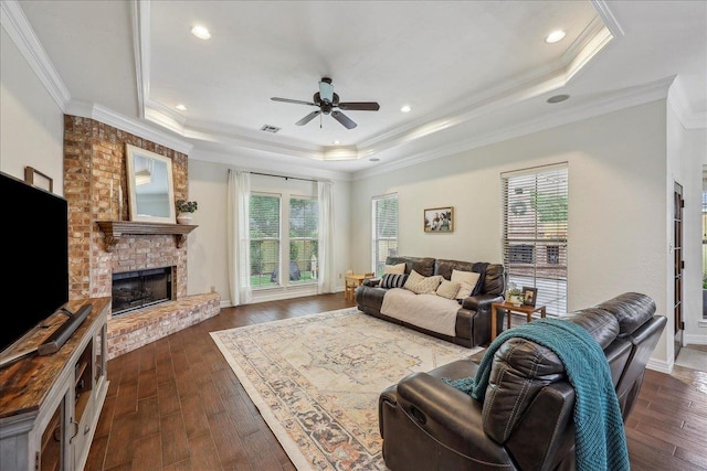 living area featuring a ceiling fan, a tray ceiling, visible vents, and dark wood finished floors