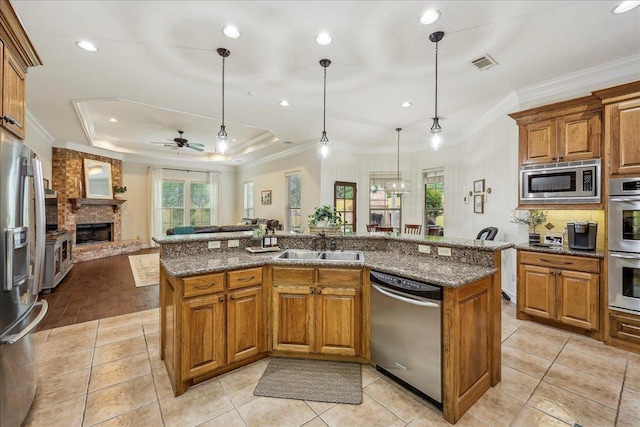kitchen featuring visible vents, a fireplace, a center island with sink, brown cabinets, and stainless steel appliances