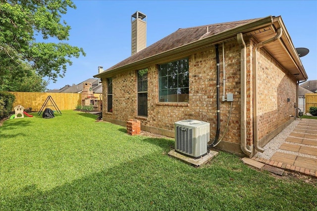 back of house with fence, brick siding, central AC unit, a chimney, and a lawn