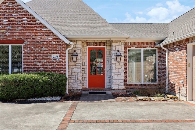 entrance to property featuring stone siding, a shingled roof, and brick siding