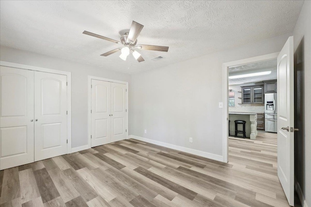 42252 State Highway 87, Orange, TX 77632 - unfurnished bedroom with stainless steel fridge with ice dispenser, light wood-style floors, two closets, a textured ceiling, and ceiling fan