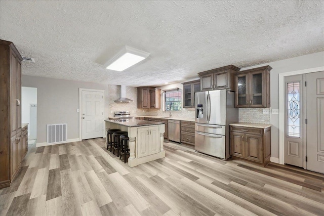 42252 State Highway 87, Orange, TX 77632 - kitchen with appliances with stainless steel finishes, wall chimney range hood, light wood-style flooring, tasteful backsplash, and glass insert cabinets