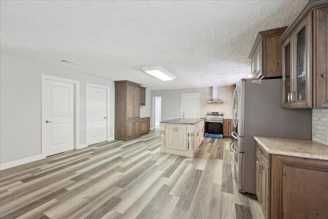 42252 State Highway 87, Orange, TX 77632 - kitchen with appliances with stainless steel finishes, wall chimney range hood, light wood finished floors, a textured ceiling, and glass insert cabinets