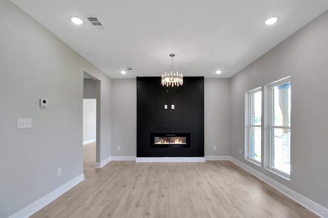 unfurnished living room with light hardwood / wood-style floors, a fireplace, and an inviting chandelier