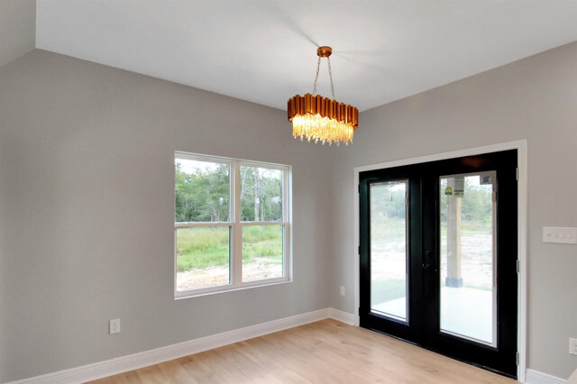 empty room featuring french doors, light wood-type flooring, and an inviting chandelier