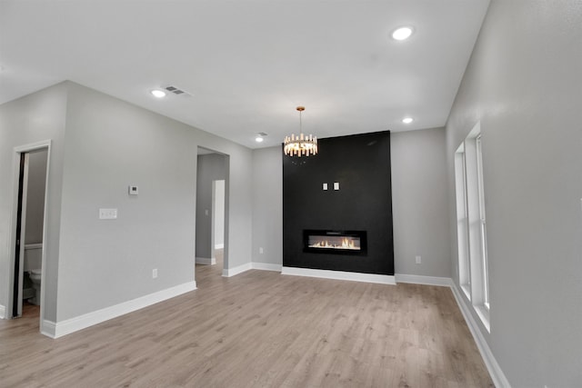 unfurnished living room featuring a fireplace, a notable chandelier, and light wood-type flooring