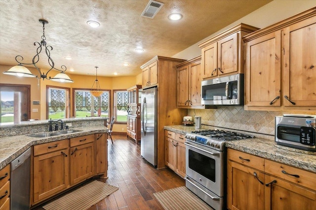 kitchen with pendant lighting, sink, dark wood-type flooring, stainless steel appliances, and decorative backsplash