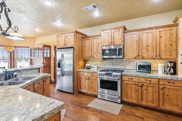 kitchen featuring sink, appliances with stainless steel finishes, pendant lighting, light stone countertops, and decorative backsplash