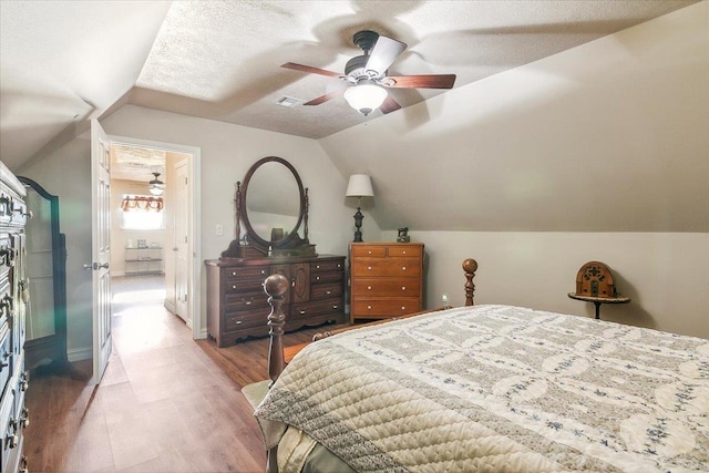 bedroom with vaulted ceiling, wood-type flooring, a textured ceiling, and ceiling fan