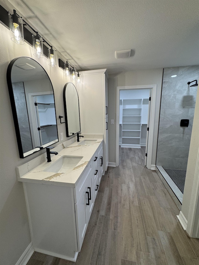 bathroom featuring a sink, tiled shower, a textured ceiling, and visible vents