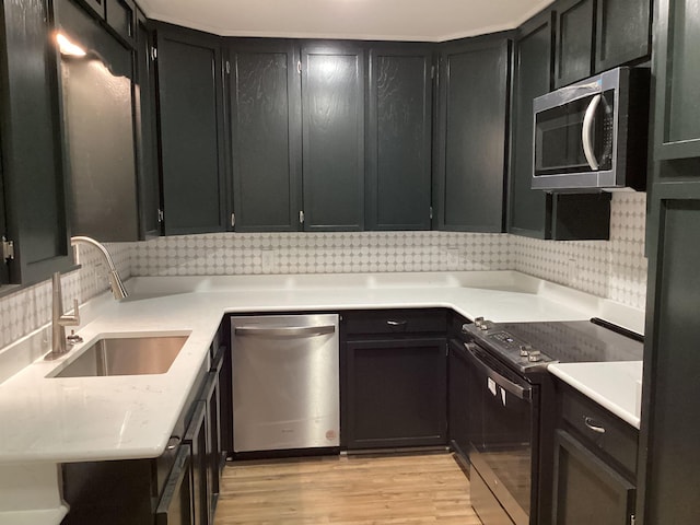 kitchen featuring decorative backsplash, light countertops, appliances with stainless steel finishes, a sink, and light wood-type flooring