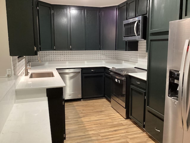 kitchen featuring light countertops, tasteful backsplash, light wood-type flooring, a sink, and appliances with stainless steel finishes