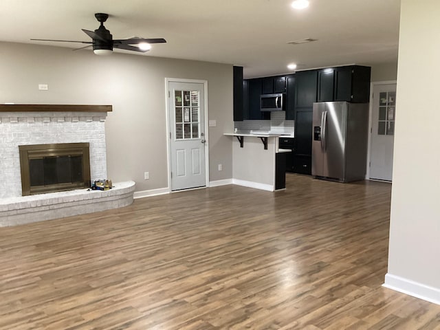 unfurnished living room with visible vents, baseboards, a fireplace, wood finished floors, and a ceiling fan