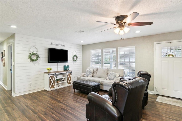 living room featuring dark wood-style flooring, visible vents, a ceiling fan, and a textured ceiling