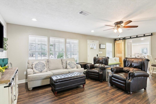 living area with ceiling fan, dark wood-type flooring, a textured ceiling, visible vents, and a barn door