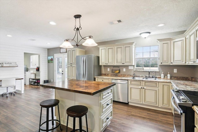 kitchen with cream cabinetry, butcher block counters, visible vents, appliances with stainless steel finishes, and a sink