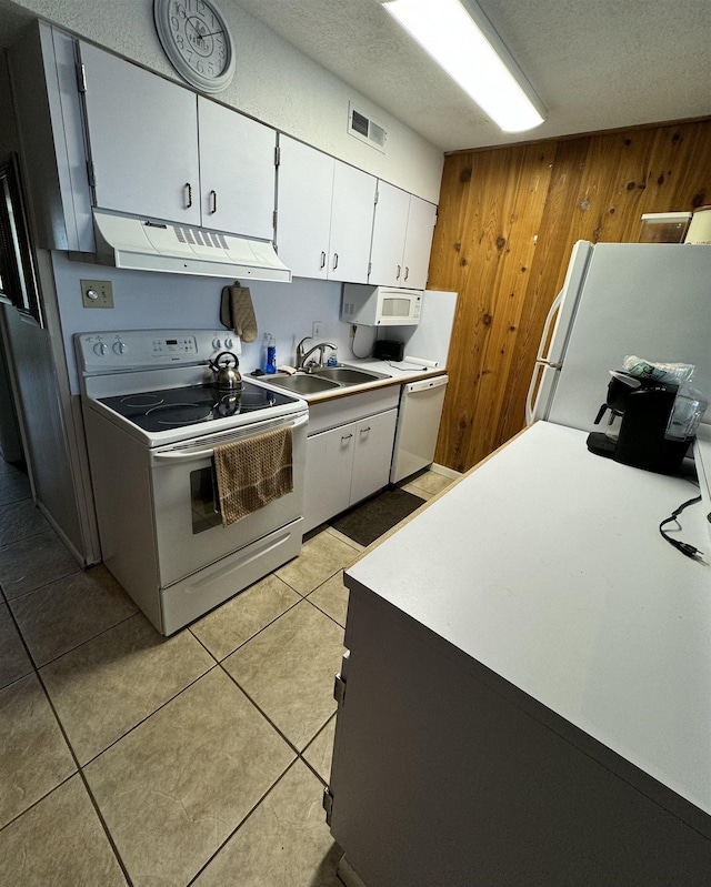 kitchen featuring sink, light tile patterned floors, white appliances, wooden walls, and white cabinets