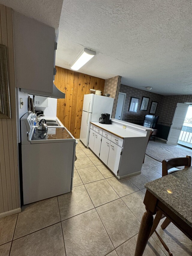 kitchen with white cabinetry, kitchen peninsula, stove, wooden walls, and light tile patterned floors