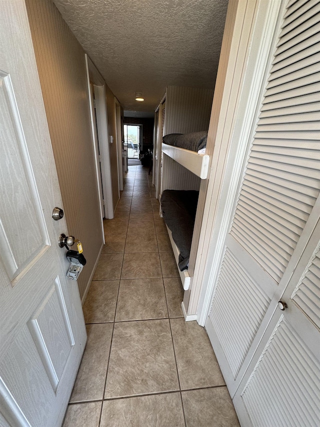 hallway featuring wood walls, light tile patterned floors, and a textured ceiling