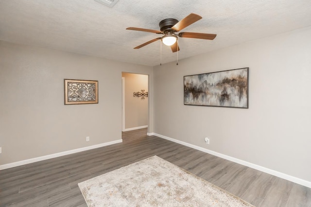 spare room featuring dark wood-style floors, a ceiling fan, baseboards, and a textured ceiling