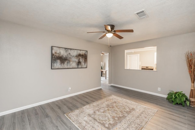 unfurnished room with a textured ceiling, wood finished floors, a ceiling fan, visible vents, and baseboards