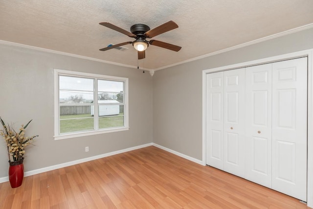 unfurnished bedroom featuring a textured ceiling, baseboards, ornamental molding, a closet, and light wood finished floors