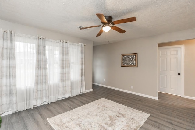 spare room with a textured ceiling, ceiling fan, dark wood finished floors, and baseboards