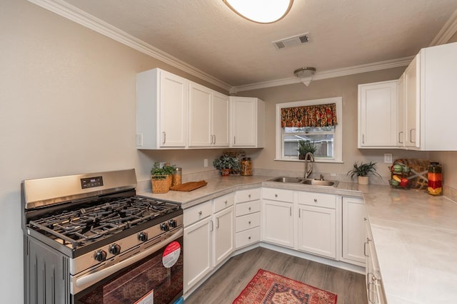 kitchen featuring white cabinets, light countertops, a sink, and stainless steel gas range oven