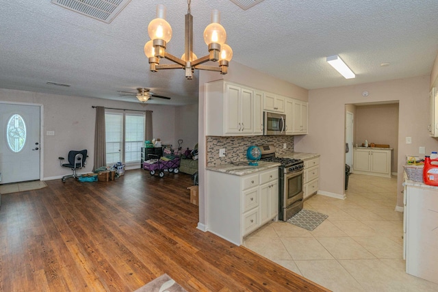 kitchen with white cabinets, appliances with stainless steel finishes, ceiling fan with notable chandelier, and pendant lighting