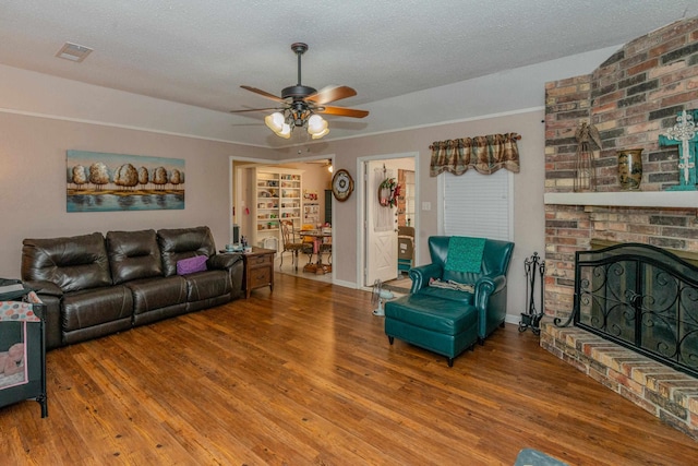 living room featuring ceiling fan, a fireplace, hardwood / wood-style floors, and a textured ceiling