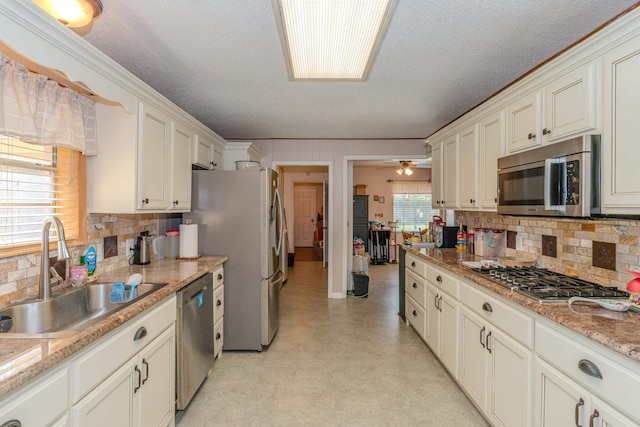 kitchen featuring decorative backsplash, a textured ceiling, stainless steel appliances, ceiling fan, and sink