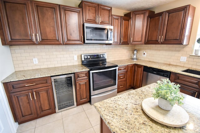 kitchen with appliances with stainless steel finishes, beverage cooler, light stone countertops, and light tile patterned floors