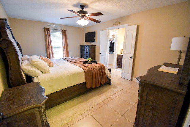 tiled bedroom with a walk in closet and ceiling fan