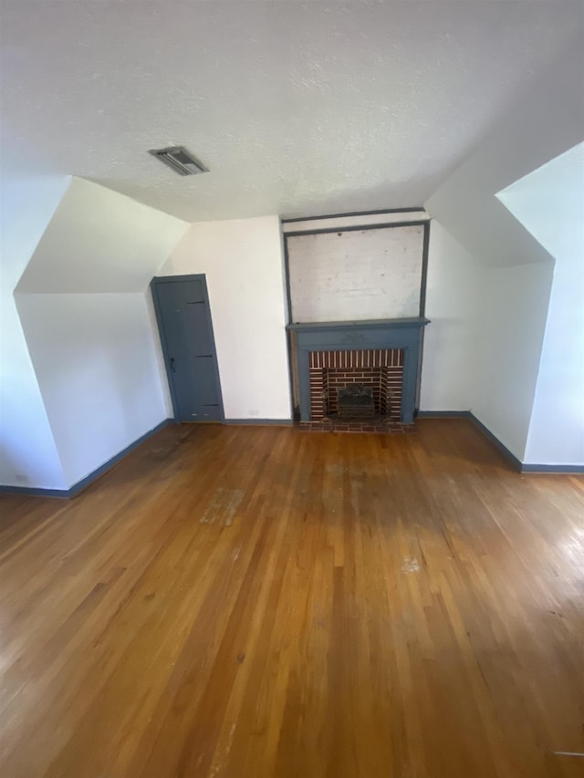 bonus room with a textured ceiling, hardwood / wood-style floors, vaulted ceiling, and a brick fireplace