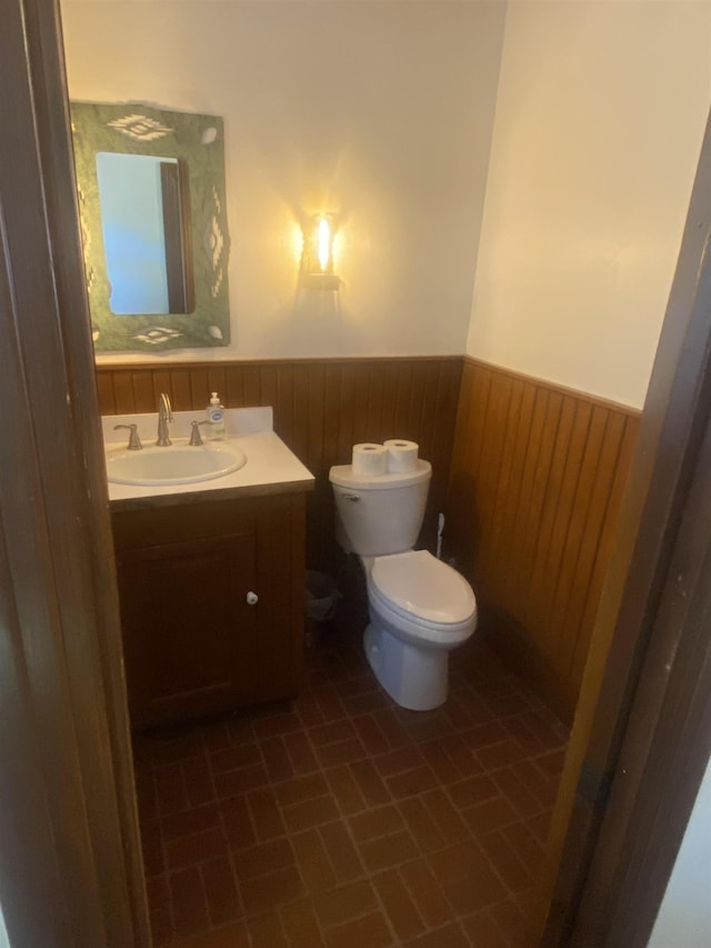 bathroom with tile patterned floors, wooden walls, vanity, and toilet