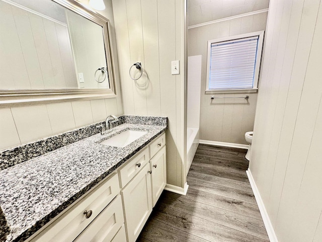 full bathroom featuring wood-type flooring, toilet, wooden walls, vanity, and ornamental molding