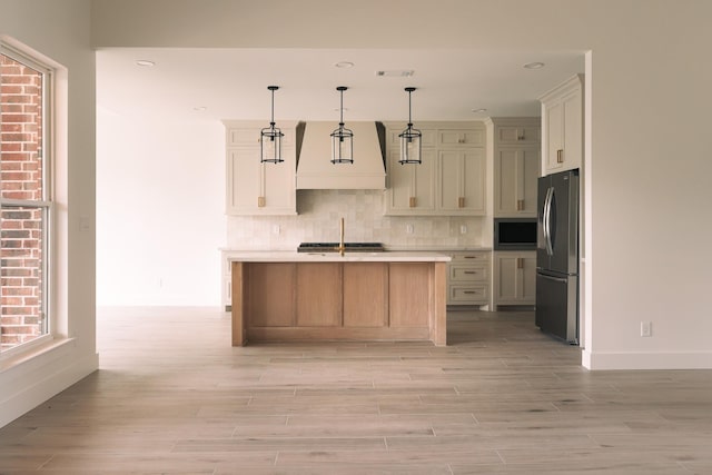 kitchen with light hardwood / wood-style flooring, an island with sink, pendant lighting, appliances with stainless steel finishes, and custom exhaust hood