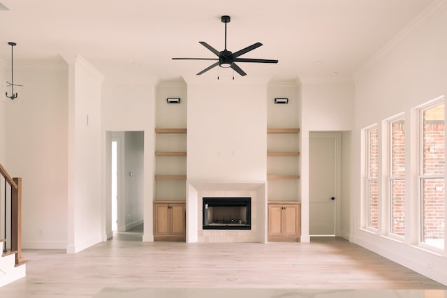 unfurnished living room with ceiling fan, built in features, ornamental molding, and light hardwood / wood-style flooring